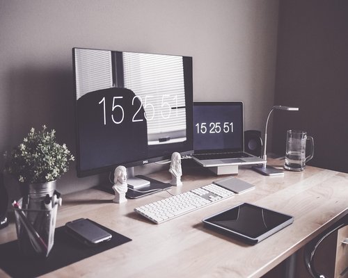 A person arranging an ergonomic home office desk setup with proper monitor height alignment